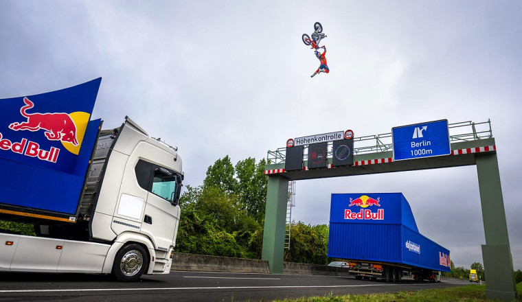 Stunt rider jumps motorcycle between two moving trucks OVER a motorway gantry - but epic backflip trick almost goes horribly wrong...